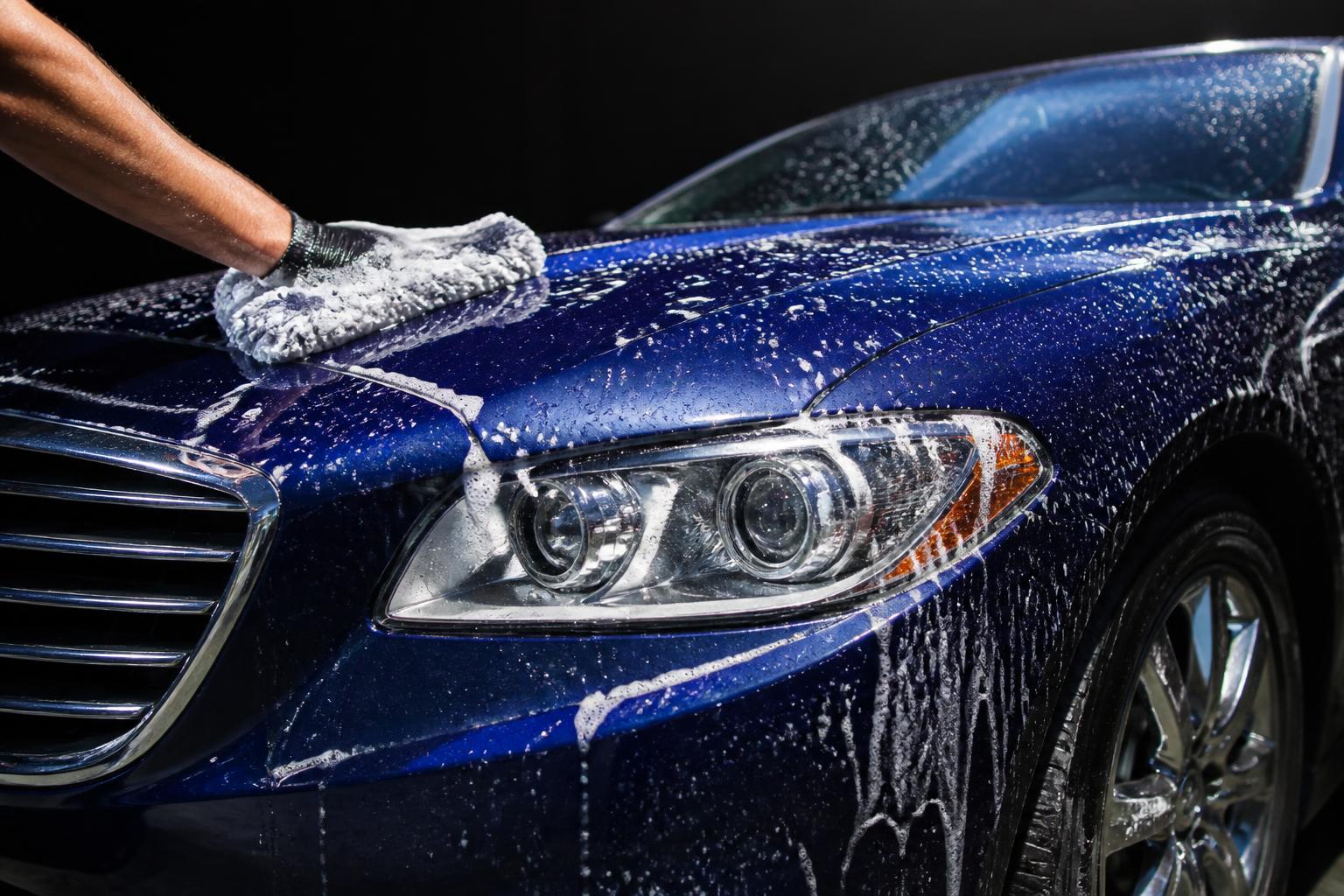 Hand washing a blue car with foam and a microfiber mitt